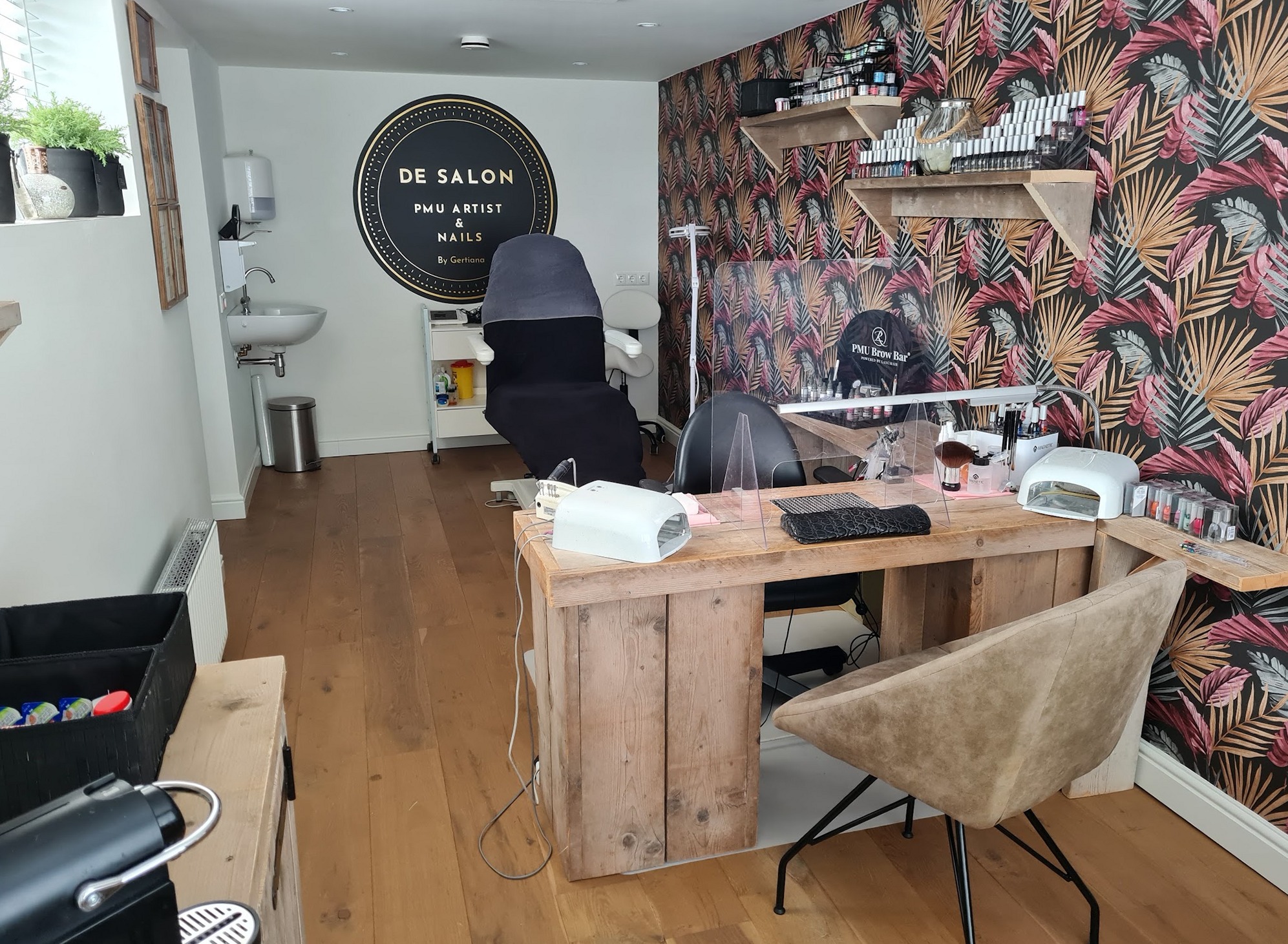 De salon met het ronde zwart-gouden logo aan de muur, de behandelstoel, het werkblad van steigerhout en het palmbehang